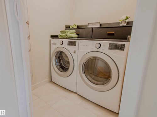 Laundry area featuring a side-by-side washer and dryer, light-toned tile flooring, and a built-in dark shelving unit with integrated storage - 5935 189 Street, Edmonton, AB - Indoor Photo Showing Laundry Room
