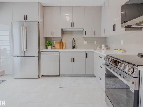 Contemporary kitchen featuring light gray cabinetry with black hardware, stainless steel appliances, a white countertop, and a tile backsplash - 5935 189 Street, Edmonton, AB - Indoor Photo Showing Kitchen
