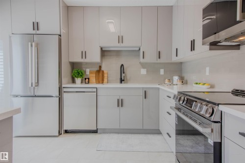 Contemporary kitchen featuring light gray cabinetry with black hardware, stainless steel appliances, white countertops, a gray tiled backsplash, and recessed lighting - 5935 189 Street, Edmonton, AB - Indoor Photo Showing Kitchen With Upgraded Kitchen