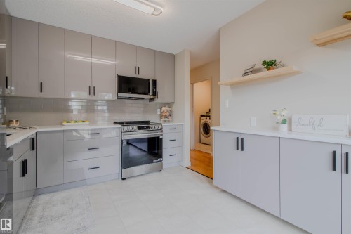 Modern kitchen featuring a stainless steel range with overhead microwave, grey high-gloss cabinetry, white countertops, and a subway tile backsplash - 5935 189 Street, Edmonton, AB - Indoor Photo Showing Kitchen
