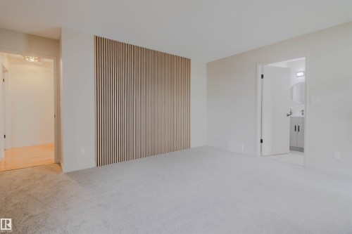 Spacious room featuring a decorative slatted accent wall, light grey carpet, and an entryway with wood-finish flooring - 5935 189 Street, Edmonton, AB - Indoor Photo Showing Other Room