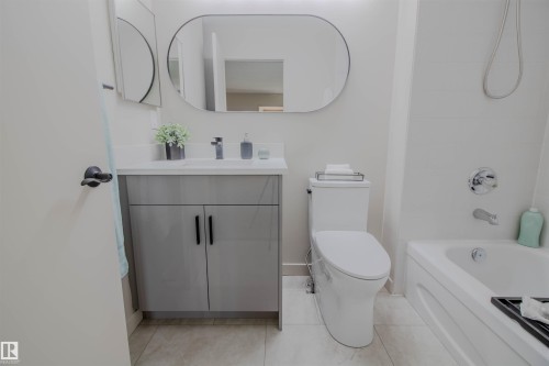Contemporary bathroom featuring a white bathtub, a modern toilet, and a vanity with a light gray cabinet, white countertop, and a rectangular undermount sink - 5935 189 Street, Edmonton, AB - Indoor Photo Showing Bathroom