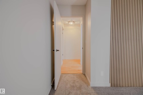 Interior hallway featuring a light wood slat accent wall, neutral-toned carpeting, and a white interior door with a black lever handle - 5935 189 Street, Edmonton, AB - Indoor Photo Showing Other Room