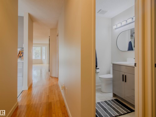Hallway featuring wood-finish flooring, leading to a bright room with large windows - 5935 189 Street, Edmonton, AB - Indoor