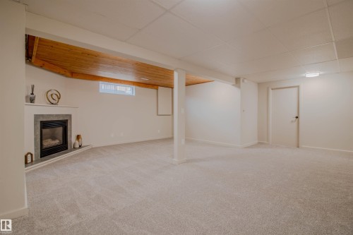 Spacious carpeted room featuring a built-in fireplace with a stone surround and hearth - 5935 189 Street, Edmonton, AB - Indoor Photo Showing Basement