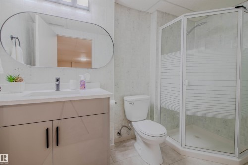 Bathroom featuring a frameless oval mirror, single vanity with light-colored countertop, corner shower with frosted glass, and neutral wall tiling - 5935 189 Street, Edmonton, AB - Indoor Photo Showing Bathroom