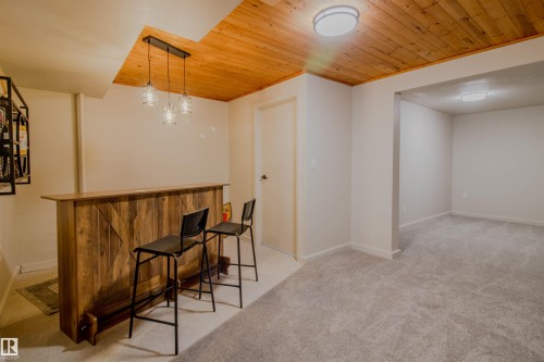 Custom-built wet bar featuring a wood-finish facade and countertop, illuminated by a three-light pendant fixture - 5935 189 Street, Edmonton, AB - Indoor Photo Showing Other Room