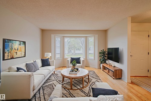 Bright living space featuring a bay window with multiple panes, light wood-finish flooring, and neutral wall tones - 5935 189 Street, Edmonton, AB - Indoor Photo Showing Living Room