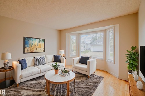 Living area featuring a prominent bay window, light wood-finish flooring, neutral wall tones, and a textured ceiling - 5935 189 Street, Edmonton, AB - Indoor Photo Showing Living Room