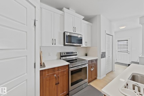 Modern kitchen featuring two-tone cabinetry, stainless steel appliances, white hexagonal tile backsplash, and light countertops - 1231 Watt Drive, Edmonton, AB - Indoor Photo Showing Kitchen