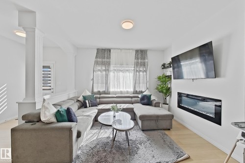 Open-concept living area featuring light wood-finish flooring, white walls, and a built-in linear electric fireplace - 1231 Watt Drive, Edmonton, AB - Indoor Photo Showing Living Room With Fireplace