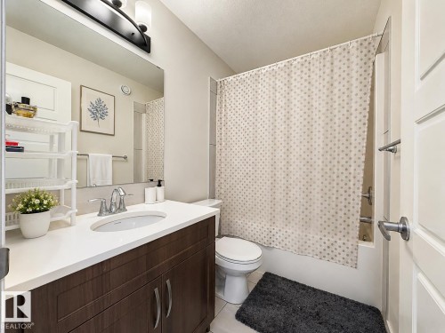 Bathroom featuring a dark wood-finish vanity with a white countertop and undermount sink, a large wall-mounted mirror, and a shower-tub combination with white tile surround - 1231 Watt Drive, Edmonton, AB - Indoor Photo Showing Bathroom