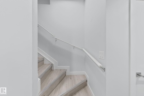 Staircase featuring wood-finish treads, white risers, and a contemporary white handrail with brushed metal brackets - 1231 Watt Drive, Edmonton, AB - Indoor With Storage