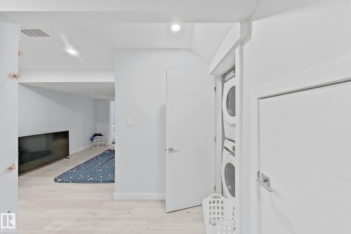 Integrated laundry closet with stacked washer and dryer, featuring modern white doors and light wood-finish flooring - 1231 Watt Drive, Edmonton, AB - Indoor Photo Showing Laundry Room