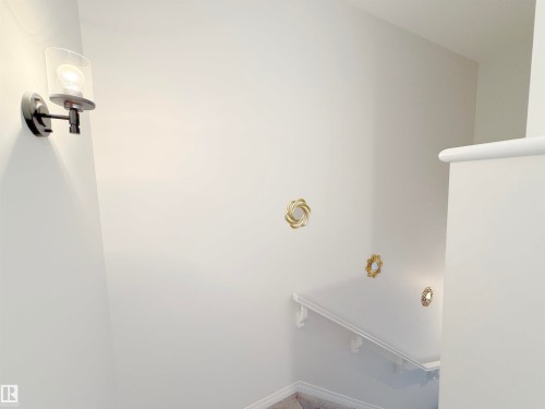 Stairwell with neutral wall tones and a matte black wall sconce featuring a clear glass shade - 1231 Watt Drive, Edmonton, AB - Indoor