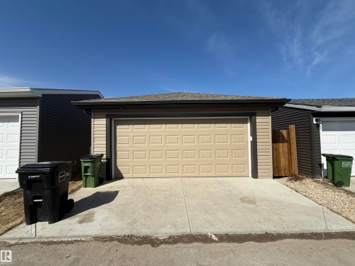 Detached garage structure featuring light beige horizontal siding, a paneled overhead door, and a shingled roof - 1231 Watt Drive, Edmonton, AB - Outdoor With Exterior