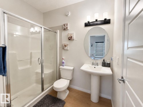 Bathroom featuring a walk-in shower with glass enclosure, a white pedestal sink with chrome faucet, an oval wall-mounted mirror, and wood-finish flooring - 1231 Watt Drive, Edmonton, AB - Indoor Photo Showing Bathroom