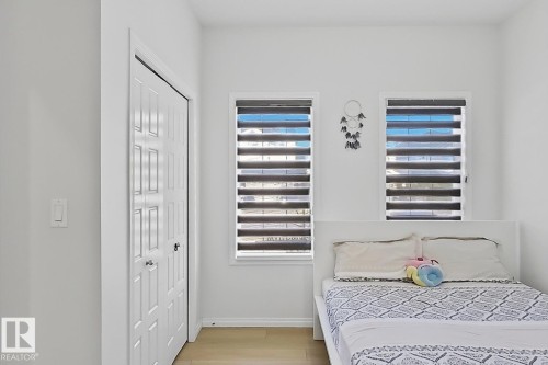 Bright interior room featuring two windows with horizontal blinds, light wood-finish flooring, and a bifold closet door - 1231 Watt Drive, Edmonton, AB - Indoor Photo Showing Bedroom