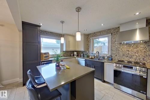 Modern kitchen featuring a central island with a solid surface countertop, two-tone cabinetry, mosaic tile backsplash, recessed lighting, and stainless steel appliances - 10 Brunswick Crescent, St. Albert, AB - Indoor Photo Showing Kitchen With Upgraded Kitchen