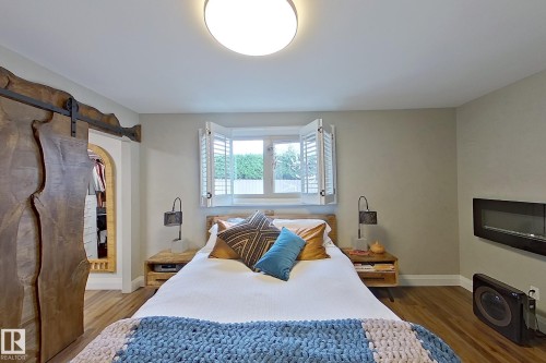 Bedroom featuring wood-finish flooring, a wall-mounted electric fireplace, and a window with plantation shutters - 10 Brunswick Crescent, St. Albert, AB - Indoor Photo Showing Bedroom
