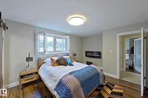 Spacious room featuring wood-finish flooring, a wall-mounted electric fireplace, and a window with white louvered shutters - 10 Brunswick Crescent, St. Albert, AB - Indoor Photo Showing Bedroom