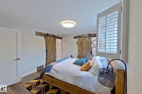 Bedroom featuring dual natural-edge live-sawn sliding barn doors, a window with plantation shutters, wood-finish flooring, and a contemporary flush-mount ceiling light - 10 Brunswick Crescent, St. Albert, AB - Indoor Photo Showing Bedroom