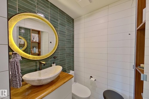 Contemporary bathroom featuring a unique stone vessel sink, a wood-finish vanity top, and a backlit oval mirror - 10 Brunswick Crescent, St. Albert, AB - Indoor Photo Showing Bathroom