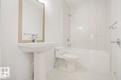 Bright bathroom featuring a pedestal sink, framed mirror, and a modern toilet - 