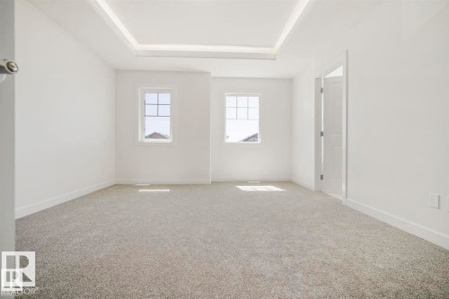 Spacious room featuring light gray carpeting, two sash windows with grilles, a tray ceiling, white baseboards, and a white interior door - 151 Kidd Crescent, Leduc, AB - Indoor Photo Showing Other Room