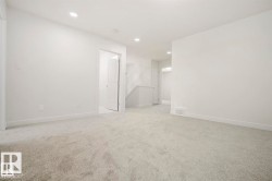 Spacious interior room with light grey carpeting, white painted walls, recessed lighting, and white baseboards - 