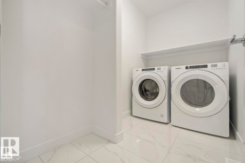Laundry area featuring a front-loading washer and dryer set, white wall shelving, and white tile flooring - 151 Kidd Crescent, Leduc, AB - Indoor Photo Showing Laundry Room