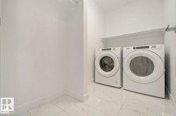 Laundry area featuring a front-loading washer and dryer set, white wall shelving, and white tile flooring - 