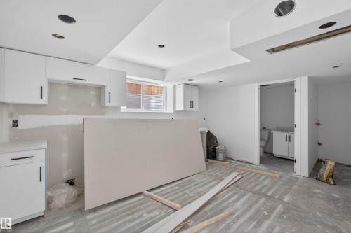 Unfinished interior space featuring white cabinetry with black hardware, a window with horizontal blinds, recessed lighting, and an adjacent unfinished bathroom - 151 Kidd Crescent, Leduc, AB - Indoor
