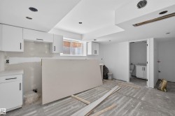 Unfinished interior space featuring white cabinetry with black hardware, a window with horizontal blinds, recessed lighting, and an adjacent unfinished bathroom - 