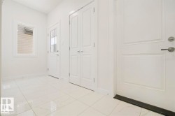 Crisp white interior space featuring large format floor tiling, a paneled entry door with modern hardware, and a small window - 