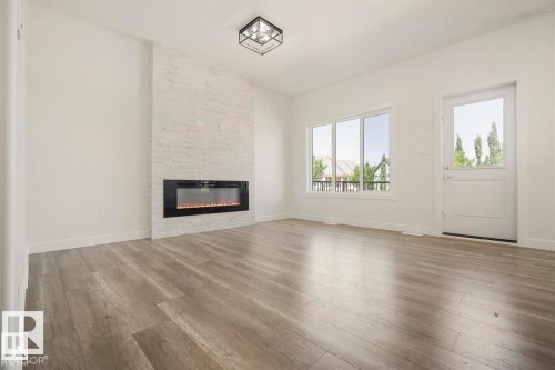 Spacious room featuring wood-finish flooring, a contemporary fireplace with a stone-finish surround, multiple windows providing natural light, and a modern ceiling light fixture - 151 Kidd Crescent, Leduc, AB - Indoor Photo Showing Living Room With Fireplace