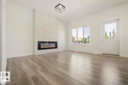 Spacious room featuring wood-finish flooring, a contemporary fireplace with a stone-finish surround, multiple windows providing natural light, and a modern ceiling light fixture - 
