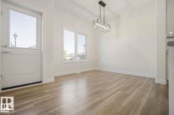Spacious room featuring wood-finish flooring, crisp white walls, and a contemporary linear chandelier - 