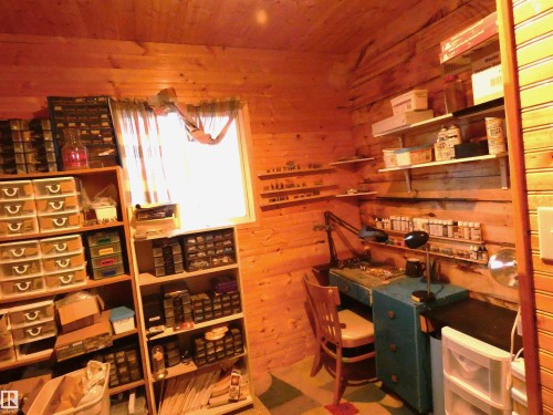 Wood-paneled room featuring built-in shelving, a light-colored window frame & dedicated workspace--Currently being used as a hobby space, this is a 2nd bedroom. Although it is smaller, there is room for perhaps bunk beds? Room is L-shaped with a window. - 307 Willow Place, Rural Barrhead County, AB 