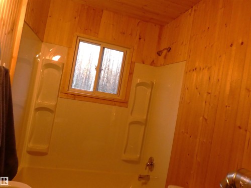 Bathroom featuring wood-paneled walls and ceiling, a white shower/tub combination, and a window with a wood trim - 307 Willow Place, Rural Barrhead County, AB 