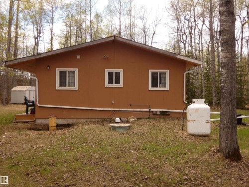 Brown exterior siding with three white-framed windows, white gutters, and a sloped roofline. Propane tank is estimated to be 200-250 gallons. It is owned and not rented. - 307 Willow Place, Rural Barrhead County, AB 