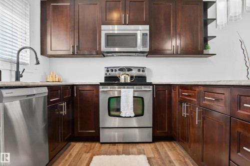 Kitchen featuring dark wood cabinetry, stainless steel appliances, a black gooseneck faucet, and wood-finish flooring - 14522 56 Street, Edmonton, AB - Indoor Photo Showing Kitchen With Stainless Steel Kitchen