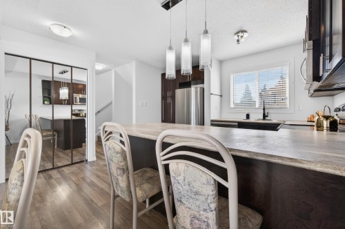 Kitchen featuring an extended island with a stone-finish look countertop, dark wood-finish cabinetry, stainless steel appliances, and wood-finish flooring - 14522 56 Street, Edmonton, AB - Indoor
