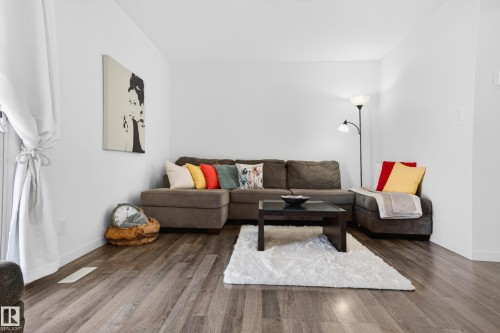 Spacious living area featuring wood-finish flooring, white walls, and a large window with white tie-back drapes - 14522 56 Street, Edmonton, AB - Indoor Photo Showing Living Room