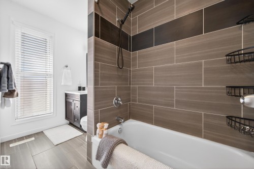 Contemporary bathroom featuring a bathtub with a tiled shower surround, large format wall tiles, and a dark wood-finish vanity with a white countertop - 14522 56 Street, Edmonton, AB - Indoor Photo Showing Bathroom