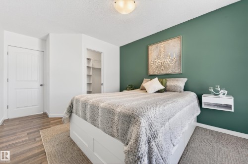 Bedroom featuring a green accent wall, wood-finish flooring, white trim, and a built-in closet with shelving - 14522 56 Street, Edmonton, AB - Indoor Photo Showing Bedroom
