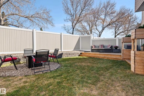 Expansive backyard featuring a manicured lawn, a gravel fire pit area, a tiered wood deck, a privacy fence, and built-in wood planters - 14522 56 Street, Edmonton, AB - Outdoor With Deck Patio Veranda
