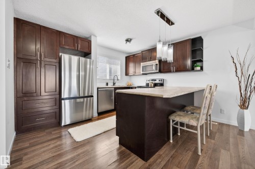Kitchen featuring dark wood cabinetry, stainless steel appliances, a light-toned countertop, and wood-finish flooring - 14522 56 Street, Edmonton, AB - Indoor Photo Showing Kitchen With Stainless Steel Kitchen With Upgraded Kitchen