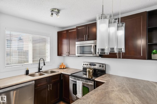 Kitchen featuring rich wood-finish cabinetry, stainless steel appliances, and stone-look countertops - 14522 56 Street, Edmonton, AB - Indoor Photo Showing Kitchen With Stainless Steel Kitchen With Double Sink