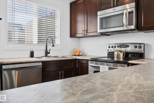 Kitchen featuring dark wood cabinetry, stainless steel appliances, a double basin sink with a black gooseneck faucet, and light-colored countertops - 14522 56 Street, Edmonton, AB - Indoor Photo Showing Kitchen With Stainless Steel Kitchen With Double Sink With Upgraded Kitchen